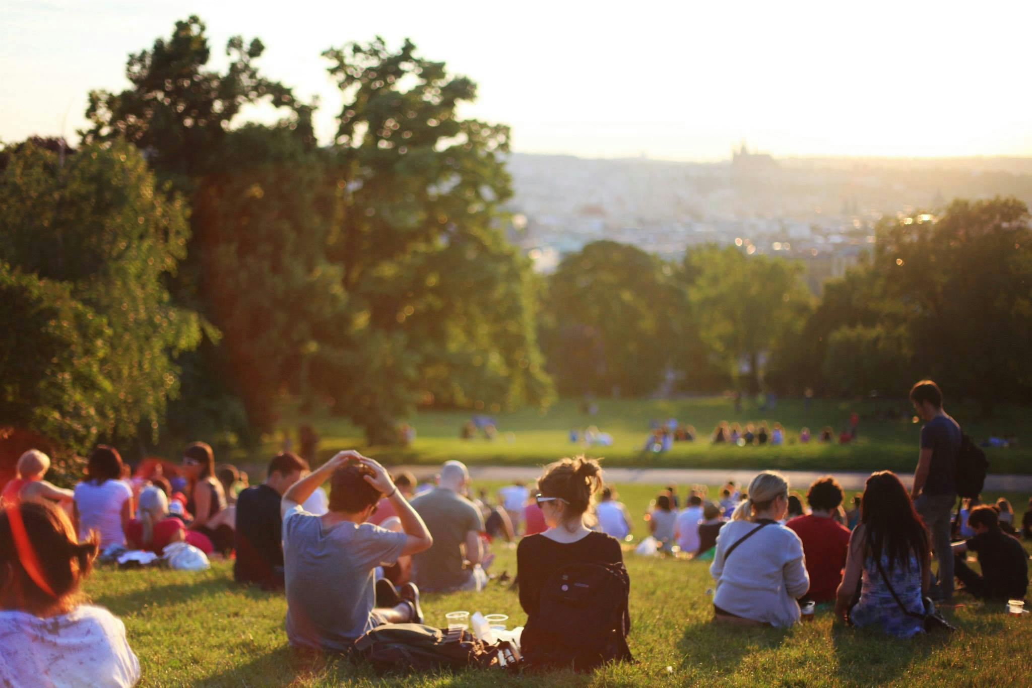 Blick auf einen Park von einem Hügel, auf denen sehr viele junge Luete sitzen und das Sommerwetter genießen.